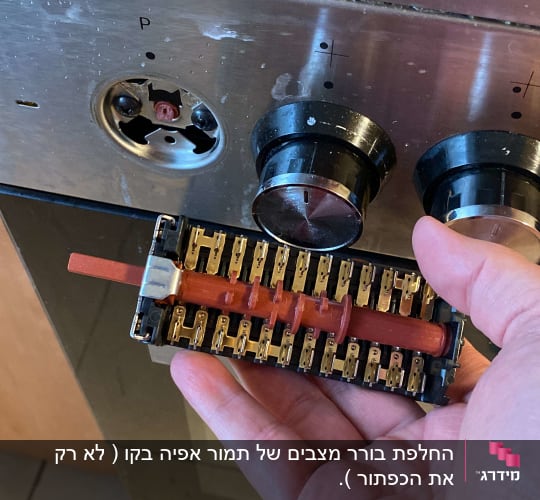 יד מחזיקה רכיב חשמלי מול כפתורי תנור